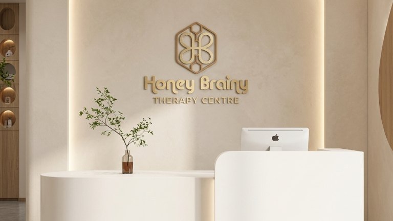 Reception at Honey Brainy Therapy Centre: a curved counter in front of a softly lit wall carrying the centre's honeycomb logo and name.
